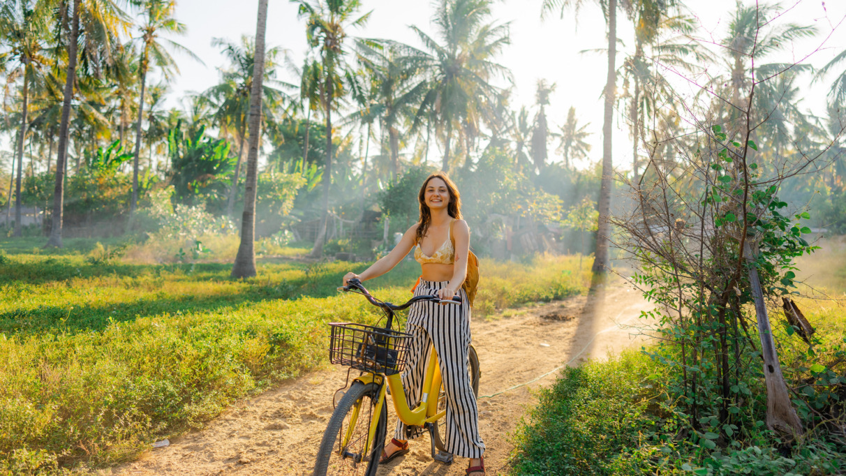 Een vrolijke vrouw die op haar fiets door een kokosnootbos op Gili Trawangan rijdt tijdens een strandvakantie in Indonesië