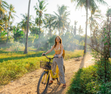 Een vrolijke vrouw die op haar fiets door een kokosnootbos op Gili Trawangan rijdt tijdens een strandvakantie in Indonesië
