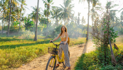 Een vrolijke vrouw die op haar fiets door een kokosnootbos op Gili Trawangan rijdt tijdens een strandvakantie in Indonesië