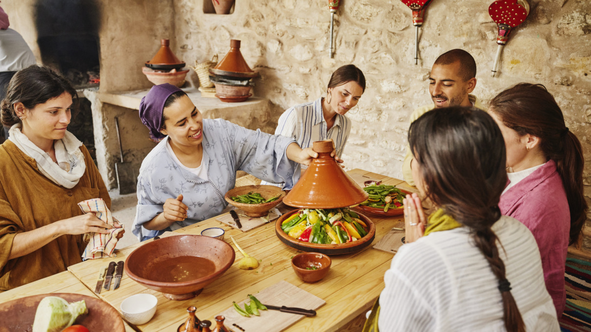 Middelbreed shot van een instructeur die een deksel op een door de studenten gemaakte tajine legt, voordat deze in een houtgestookte oven wordt bereid