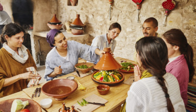 Middelbreed shot van een instructeur die een deksel op een door de studenten gemaakte tajine legt, voordat deze in een houtgestookte oven wordt bereid