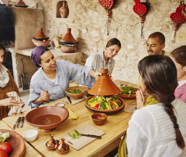 Middelbreed shot van een instructeur die een deksel op een door de studenten gemaakte tajine legt, voordat deze in een houtgestookte oven wordt bereid