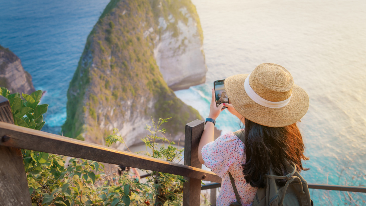 Een jonge vrouw die bij zonsondergang foto’s maakt bij het uitkijkpunt aan het Kelingking-strand. Een beroemde plek op het eiland Nusa Penida, Bali, Indonesië.