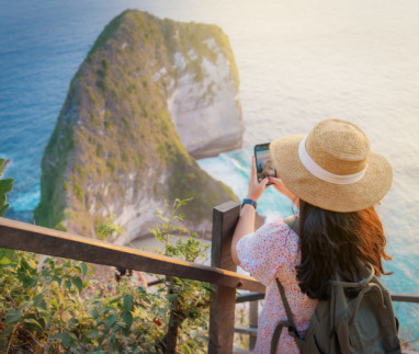 Een jonge vrouw die bij zonsondergang foto’s maakt bij het uitkijkpunt aan het Kelingking-strand. Een beroemde plek op het eiland Nusa Penida, Bali, Indonesië.