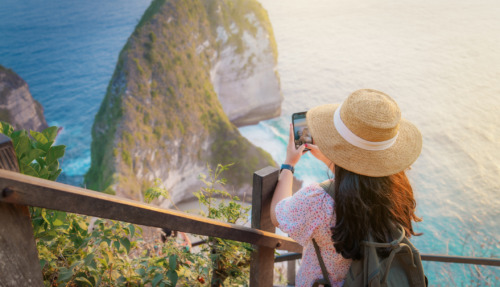 Een jonge vrouw die bij zonsondergang foto’s maakt bij het uitkijkpunt aan het Kelingking-strand. Een beroemde plek op het eiland Nusa Penida, Bali, Indonesië.
