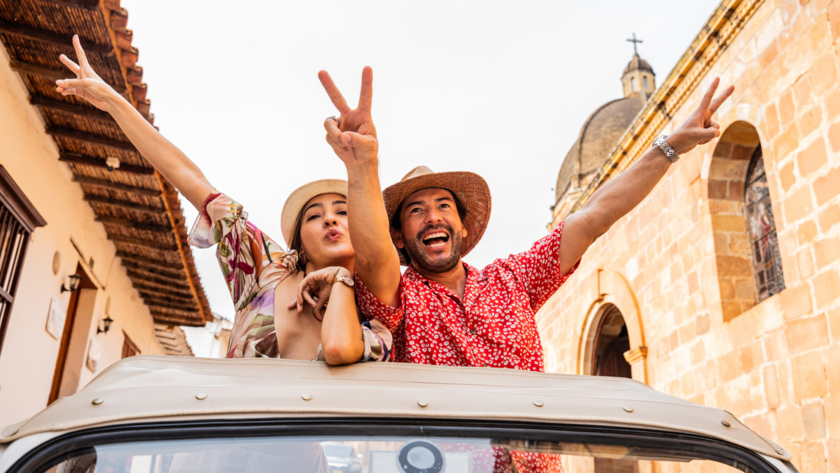 Toeristenstel maakt vredesteken met de vingers terwijl ze uit het dak van een cabrio hangen