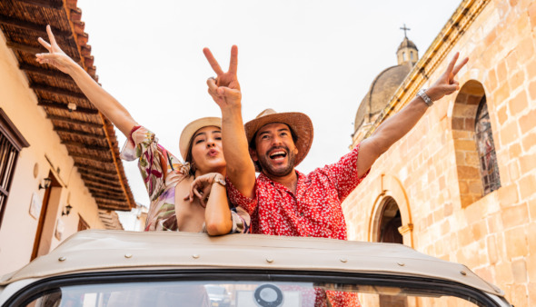 Toeristenstel maakt vredesteken met de vingers terwijl ze uit het dak van een cabrio hangen