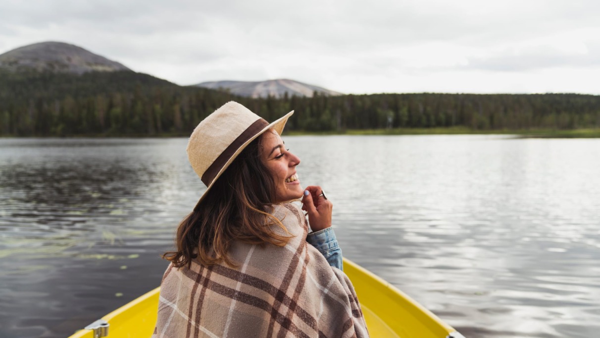 Lachende vrouw in een gele boot op een meer, omringd door bergen en bossen