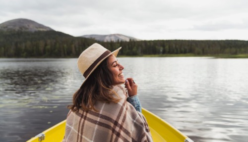 Lachende vrouw in een gele boot op een meer, omringd door bergen en bossen