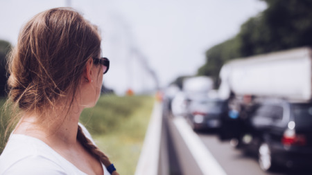 Vrouw staat in de file bij de vangrail te wachten tot het verkeer weer gaat rijden