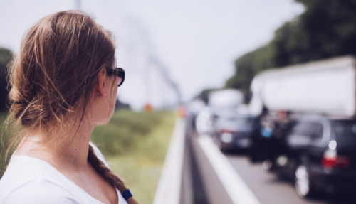 Vrouw staat in de file bij de vangrail te wachten tot het verkeer weer gaat rijden