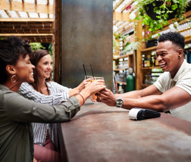 Mannelijke bartender serveert twee vrouwelijke klanten hun cocktails aan de bar