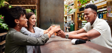Mannelijke bartender serveert twee vrouwelijke klanten hun cocktails aan de bar