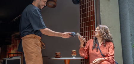 Mannelijke ober in Australië geeft glimlachend pinapparaat aan vrouwelijke klant op het terras