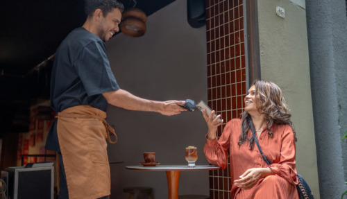 Mannelijke ober in Australië geeft glimlachend pinapparaat aan vrouwelijke klant op het terras