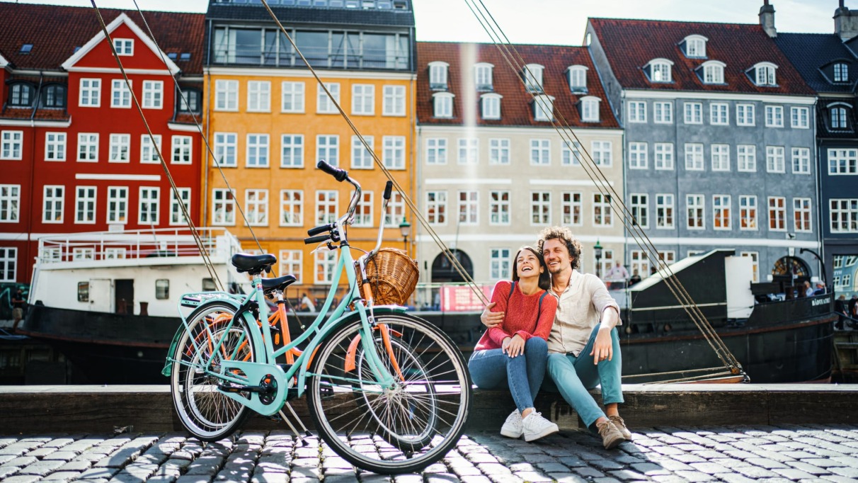 Een lachend stel geniet van een zonnige dag in de kleurrijke Nyhavn-haven van Kopenhagen, de gelukkigste stad ter wereld volgens de Happy City Index 2025.