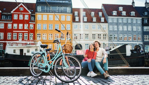 Een lachend stel geniet van een zonnige dag in de kleurrijke Nyhavn-haven van Kopenhagen, de gelukkigste stad ter wereld volgens de Happy City Index 2025.