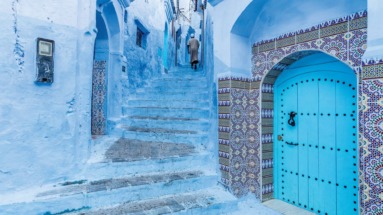 Smalle straat in de blauwgeschilderde medina van Chefchaouen, Marokko, met traditionele tegels en een blauwe deur.