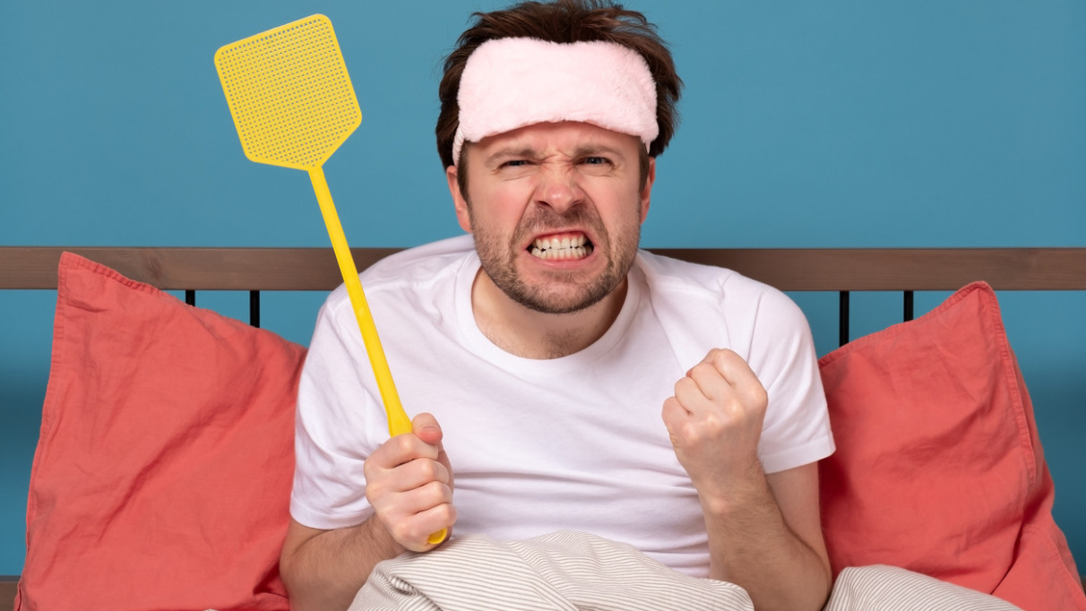 man holding a fly swatter wanting to kill annoying mosquito
