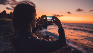 Woman at the beach photographing the sunset