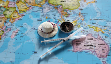 A compass with two disposable syringes and travel cap on world map.