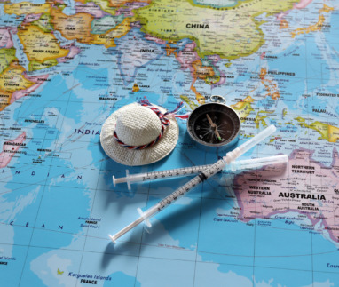 A compass with two disposable syringes and travel cap on world map.