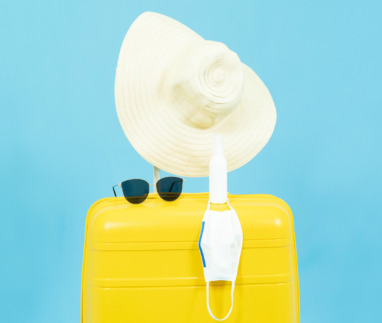 Summer holidays,vacation and travel concept.Yellow Suitcase or luggage bag,sun hat,sunglasses,medical face mask and alcohol Spray,the reopening of the Tourism after the quarantine on blue background