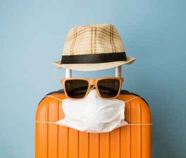 Suitcase with hat, sunglasses and protective medical mask on pastel blue background minimal creative coronavirus covid-19 travel concept.