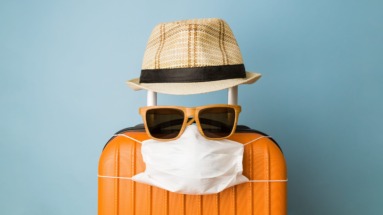 Suitcase with hat, sunglasses and protective medical mask on pastel blue background minimal creative coronavirus covid-19 travel concept.