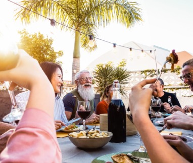 Happy family doing a dinner during sunset time outdoor – Group of diverse friends having fun dining together outside – Concept of lifestyle people, food and weekend activities