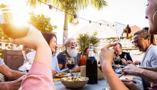 Happy family doing a dinner during sunset time outdoor – Group of diverse friends having fun dining together outside – Concept of lifestyle people, food and weekend activities
