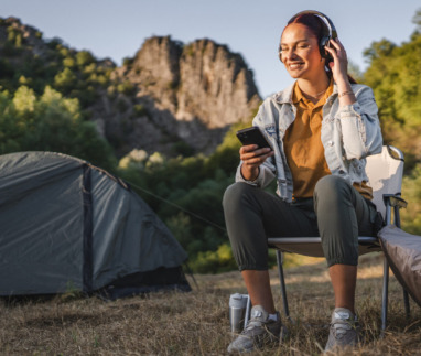 Vrouw geniet van een podcast met koptelefoon bij een tent in de natuur