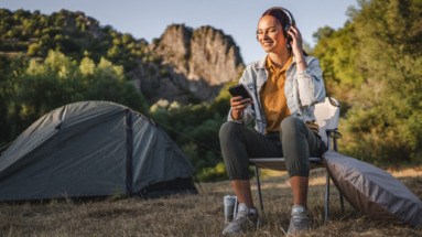 Vrouw geniet van een podcast met koptelefoon bij een tent in de natuur