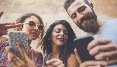 Drie jonge mensen kijken lachend op hun smartphones, bezig met een quiz of spel.