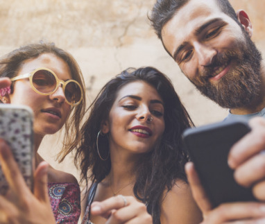 Drie jonge mensen kijken lachend op hun smartphones, bezig met een quiz of spel.