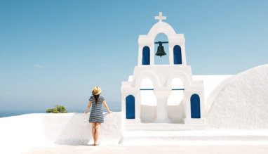 Vrouw geniet van het uitzicht bij een witte kerk met blauwe accenten op Santorini in Griekenland