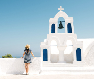 Vrouw geniet van het uitzicht bij een witte kerk met blauwe accenten op Santorini in Griekenland