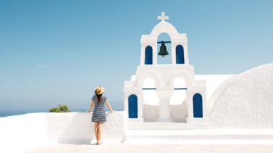 Vrouw geniet van het uitzicht bij een witte kerk met blauwe accenten op Santorini in Griekenland