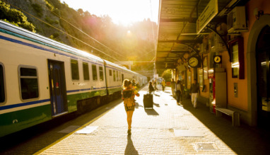Reiziger met rugzak loopt over een perron richting een trein bij zonsondergang