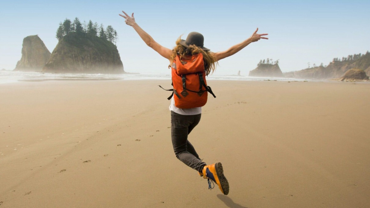 Vrouwelijke solo-reiziger met rugzak springt op een verlaten strand