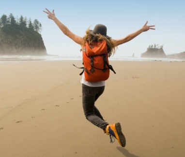 Vrouwelijke solo-reiziger met rugzak springt op een verlaten strand