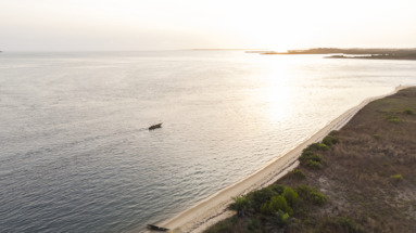 Zonsondergang aan de kust van Sierra Leone met een traditionele vissersboot op kalm water en een afgelegen zandstrand.