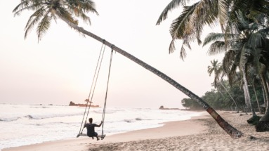 Reiziger schommelt aan een palmboom op een tropisch strand in Ghana, met de oceaan op de achtergrond.