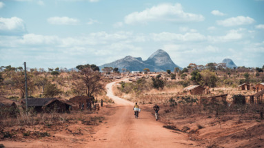 Uitzicht over een landelijke weg met traditionele hutten en bergachtig landschap in Mozambique