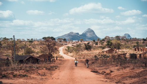 Uitzicht over een landelijke weg met traditionele hutten en bergachtig landschap in Mozambique