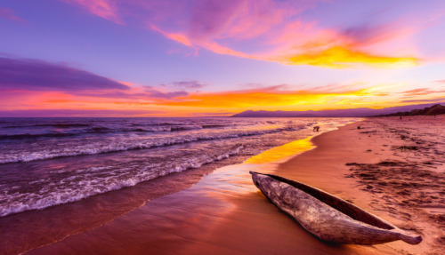 Een kleurrijke zonsondergang aan het Malawimeer met een traditionele houten kano op het strand.