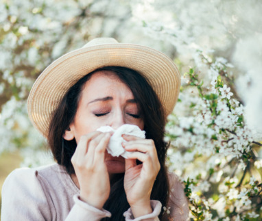 Vrouw met hoed niest in een zakdoek te midden van bloeiende bomen