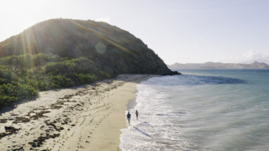 Twee mensen wandelen langs een idyllisch strand met helderblauw water op Saint Kitts en Nevis.