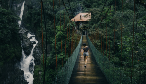 Toerist wandelt over een hangbrug met uitzicht op de Pailón del Diablo-waterval in het regenwoud van Ecuador