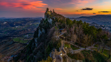 Prachtig uitzicht op een van de iconische torens van San Marino bij zonsondergang, omgeven door glooiende heuvels en een kleurrijke lucht.